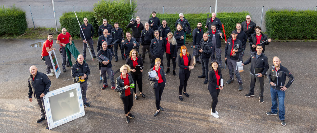 Eine Gruppe fröhlicher Menschen in Arbeitskleidung mit Werkzeugen und Bauteilen draußen
