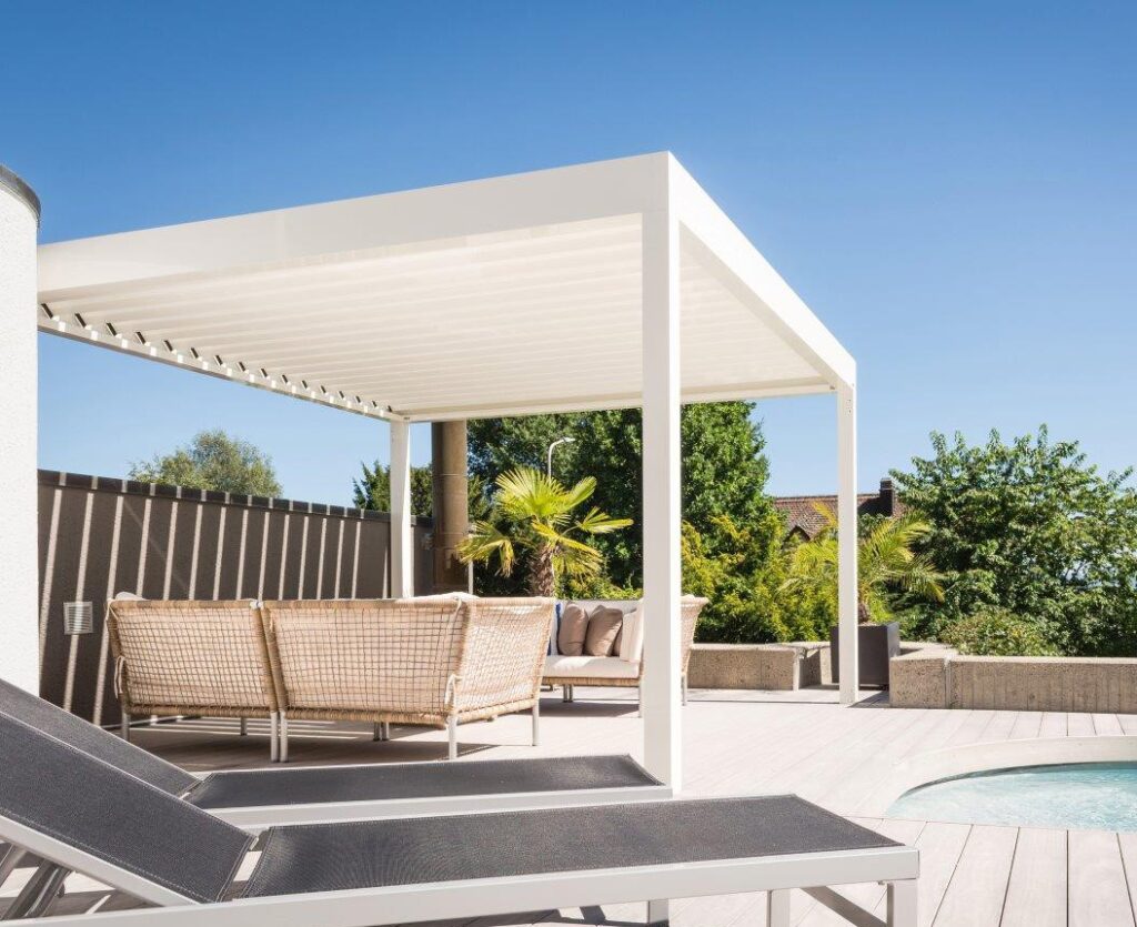 Moderne überdachte Terrasse mit weißen Möbeln, grauer Liege und blauem Pool unter klarem Himmel